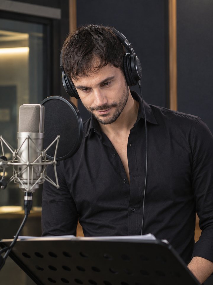 Carlos J. Pérez grabando en su cabina, con cascos y guion en el atril